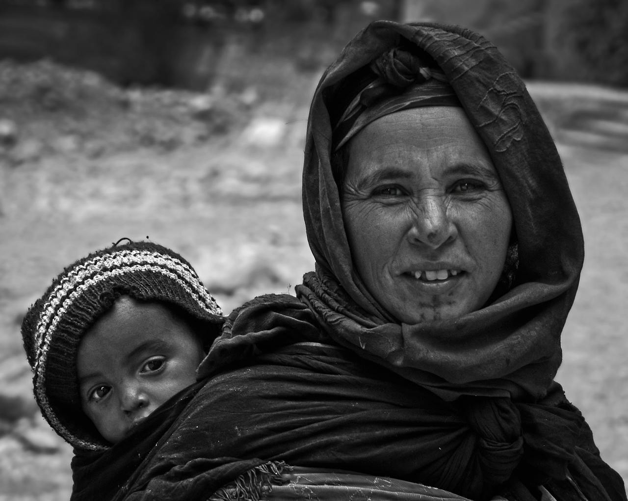 Black and white portrait of a mother carrying her child, showcasing family bonds in Morocco.